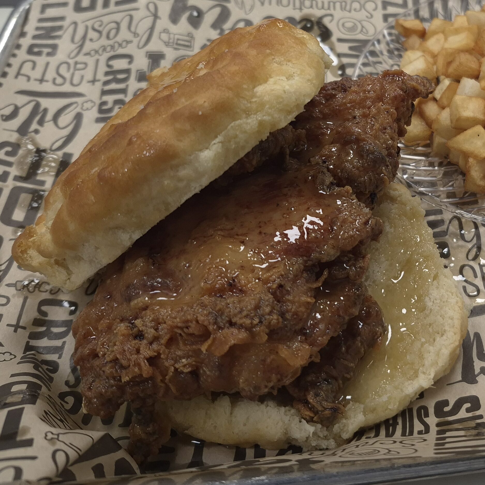 A Honey Butter Chicken Biscuit with Home Fries on a metal tray